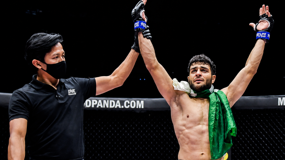 Pakistani MMA fighter in a cage fight, gloves raised after a win